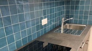 Una cocina con tope de inducción negro, un lavamanos de acero inoxidable y salpicadero de azulejos azules.