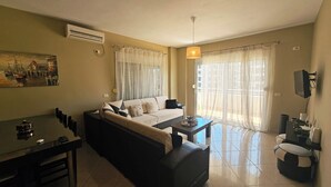 A living room with a sofa, a dining table, and a TV mounted on the wall. - Albania Dream Holidays Accommodation (Sarand)