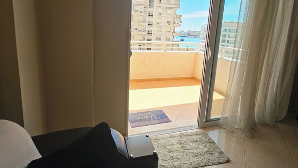 A hotel room with a sliding glass door leading to a balcony, a bed, and a small rug on the floor. - Albania Dream Holidays Accommodation (Sarand)