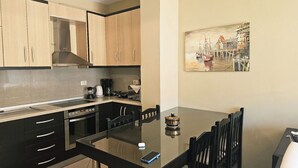 A modern kitchen with wooden cabinets, a dining table with chairs, and a painting on the wall. - Albania Dream Holidays Accommodation (Sarand)