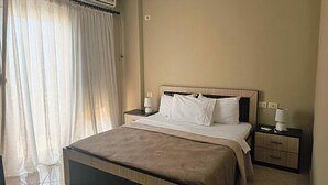 A hotel room with a bed, bedside tables, a lamp, and a window with curtains. - Albania Dream Holidays Accommodation (Sarand)
