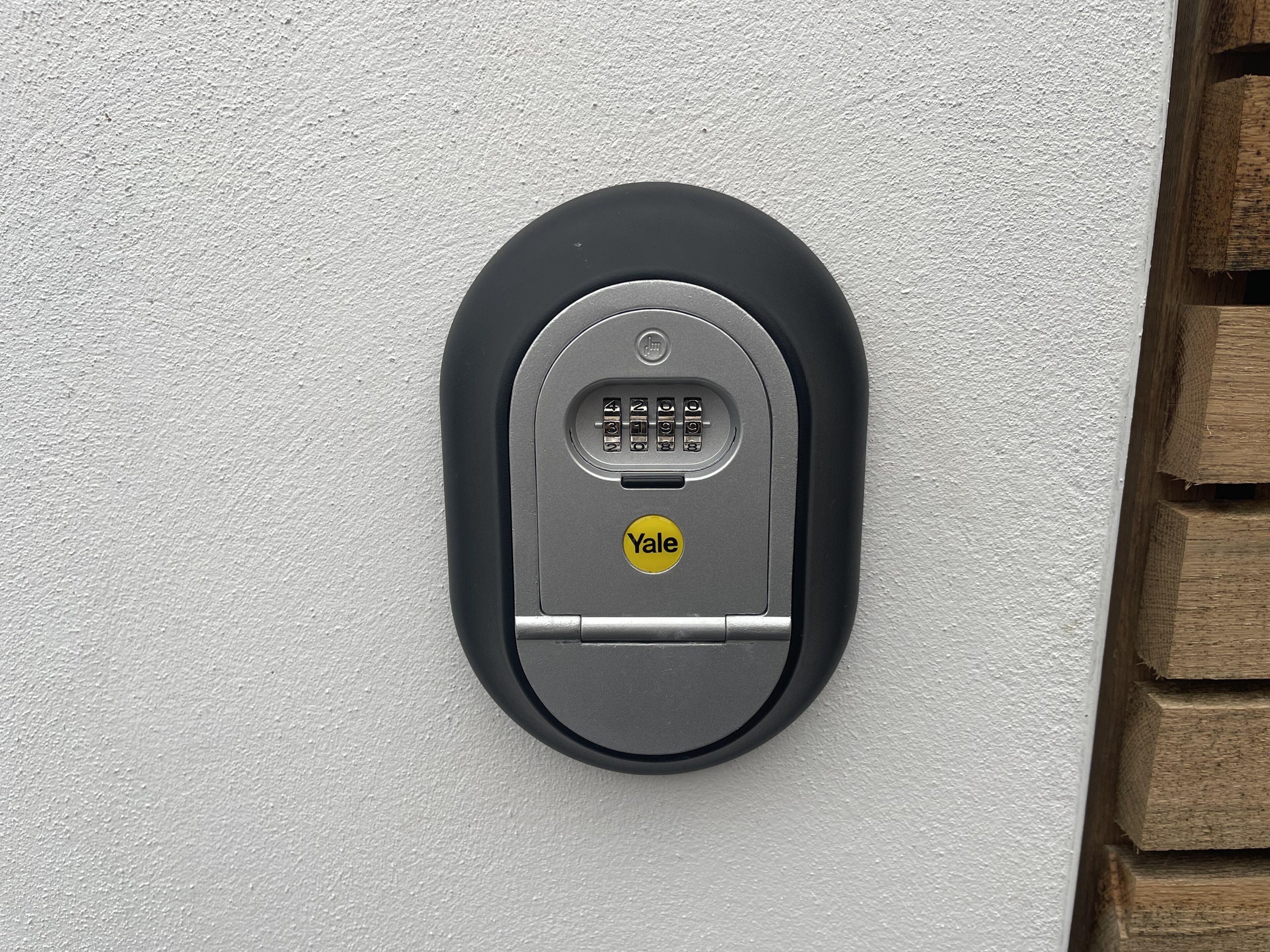 Een modern, ovaalvormig, zwart intercomsysteem bevestigd aan een witte, gestructureerde muur.