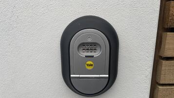 Een modern, ovaalvormig, zwart intercomsysteem bevestigd aan een witte, gestructureerde muur.