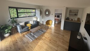 A modern living room with a sofa, coffee table, and a yellow armchair. There is a kitchen area with a counter and cabinets. - Relaxing guest house with Jacuzzi & boat hire (Staines)