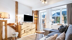 Uma sala de estar moderna com sofá, televisão, detalhes em madeira e vista para uma paisagem nevada através de grandes janelas.