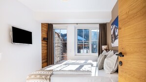 Quarto com uma cama, televisão, duas janelas e porta de madeira.