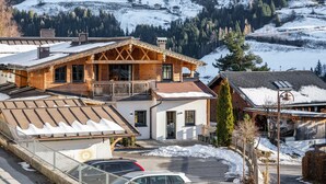 Um edifício em estilo chalé com varanda, área de estacionamento coberta e vista para uma montanha nevada.