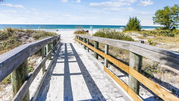 Una passerella di legno che conduce a una spiaggia, con cielo sereno e acque calme.