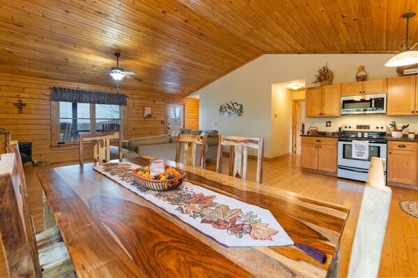 A wooden interior with a dining table, chairs, a kitchen area, and a living room with a sofa.