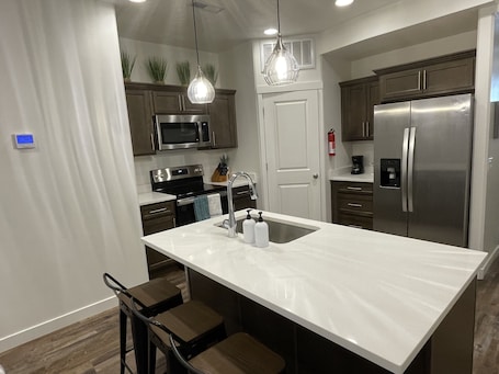 A modern kitchen with a large island, stainless steel appliances, and wooden cabinets.