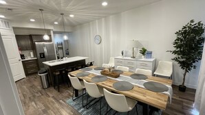 Eine moderne Küche mit einer zentralen Kochinsel, weißen Schränken und einem Essbereich mit Holztisch und Stühlen.