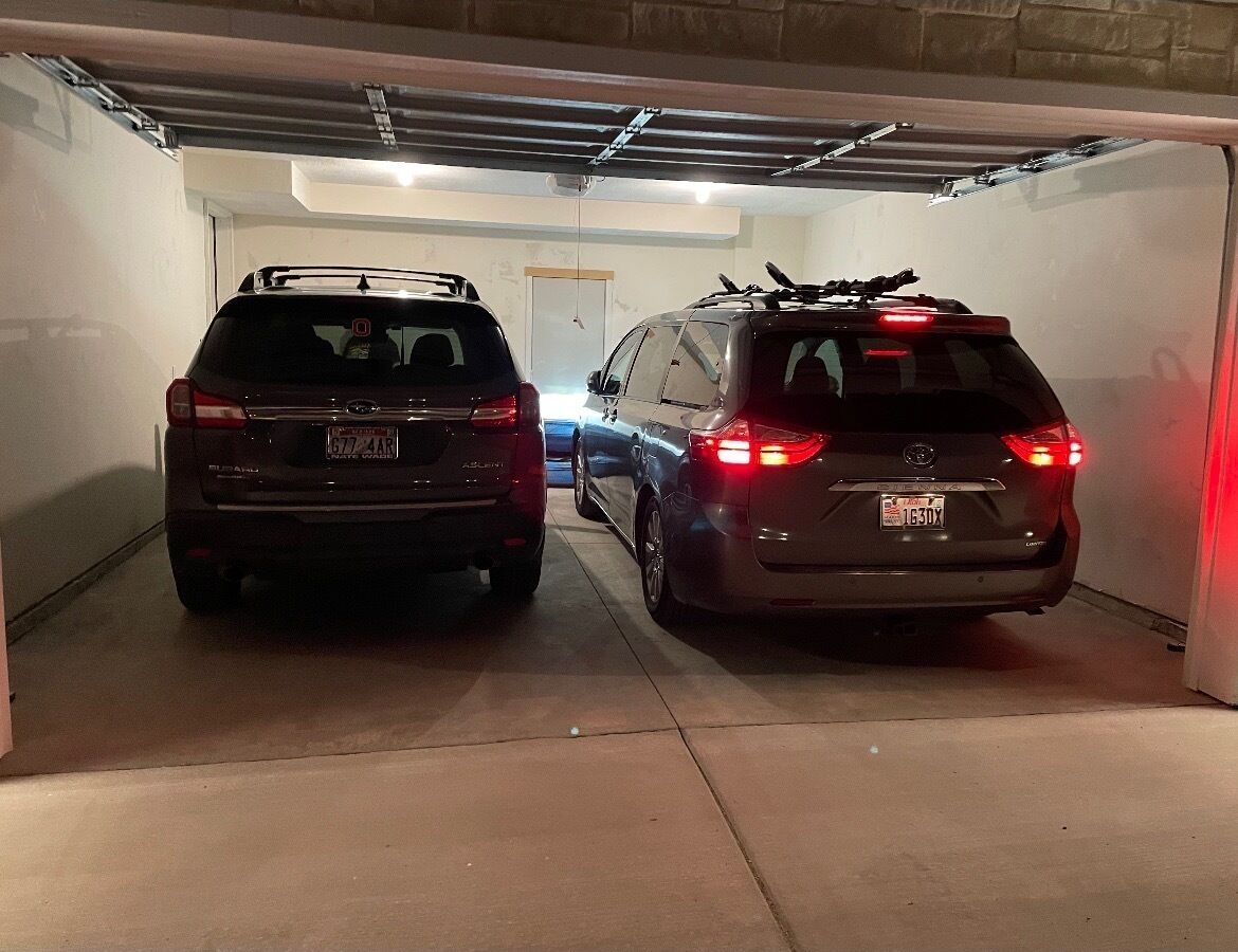 Deux voitures sont garées dans un garage dont le sol est en béton et les murs sont blancs.