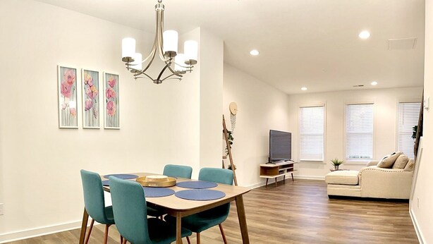 Un espace repas moderne avec une table en bois et des chaises de couleur turquoise, un lustre et des œuvres d’art accrochées aux murs.