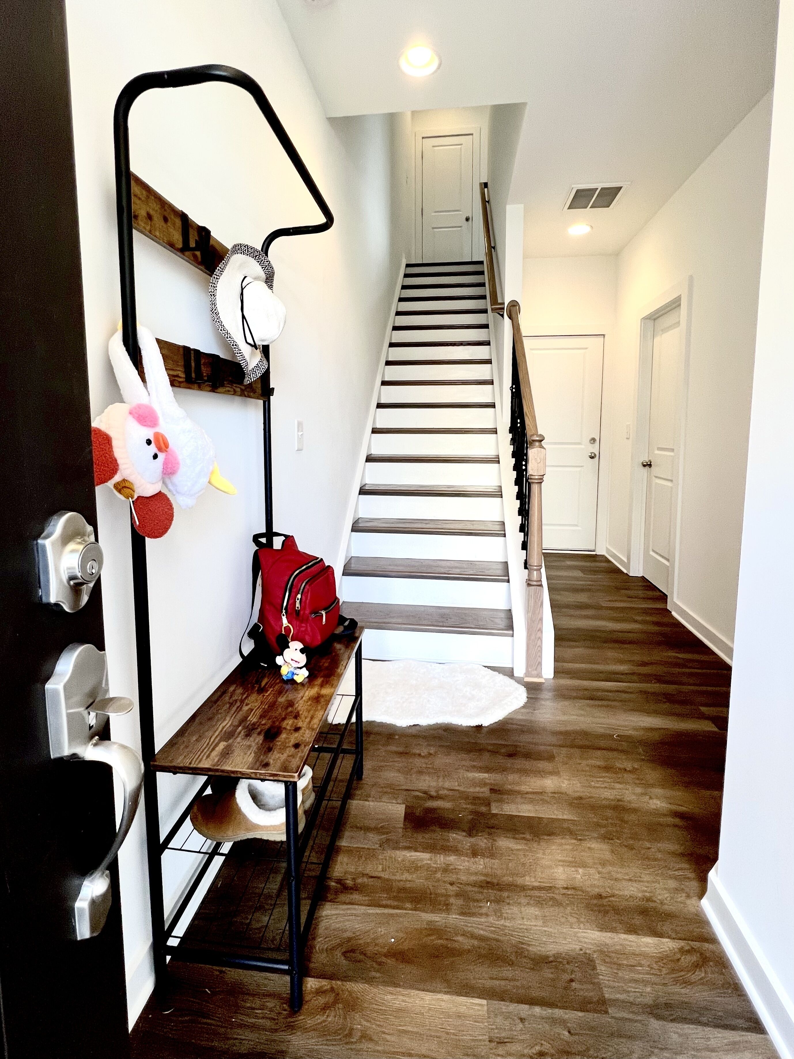 Un couloir avec un banc en bois, un sac rouge et un jouet en peluche.