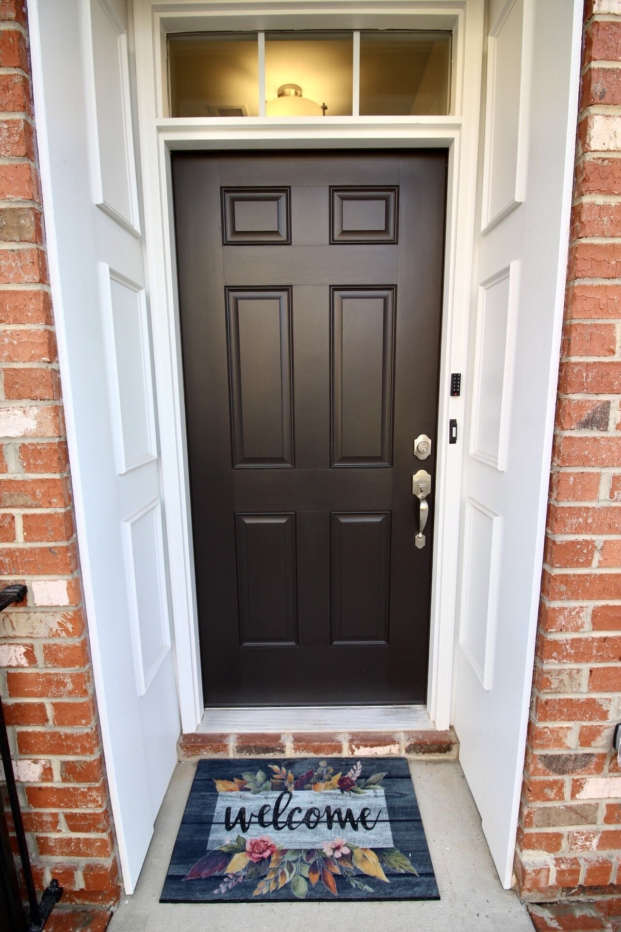 A dark brown door with a white frame, a doormat with 'welcome' written on it, and a small window above the door.