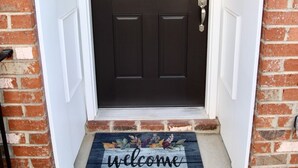 Une porte d’entrée marron foncé avec un cadre blanc, un paillasson sur lequel est écrit « bienvenue », et une petite fenêtre au-dessus de la porte.