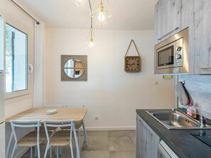 Una cocina moderna con una mesa y sillas de madera, una lámpara colgante, un reloj en la pared y un microondas empotrado.