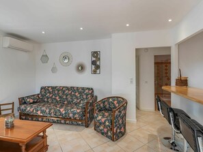 A living room with a sofa and armchair, a wooden coffee table, and a dining area with chairs.