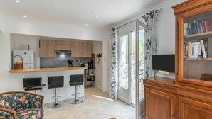 A modern kitchen with wooden cabinets, a built-in fridge, and a bar area. There is a dining area with a floral chair and a wooden table. - Beautiful apartment in villa for 3 people with WIFI, A/C, TV and terrace (Solenzara)