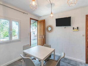 A modern room with a white table and chairs, a TV mounted on the wall, and a door leading to an outdoor area. - Lovely apartment in villa for 4 guests with A/C, WIFI and TV (Solenzara)