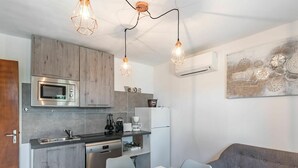 A modern kitchen with a built-in microwave, oven, and sink, a white dining table with chairs, and a gray sofa. - Cosy apartment in villa for 4 people with A/C, WIFI and TV (Solenzara)