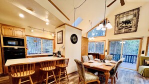 Una mesa de madera con sillas, una zona de cocina con microondas y un ventanal con vistas a un bosque.