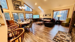 Amplia sala de estar con comedor, ventanas grandes, chimenea y televisor.