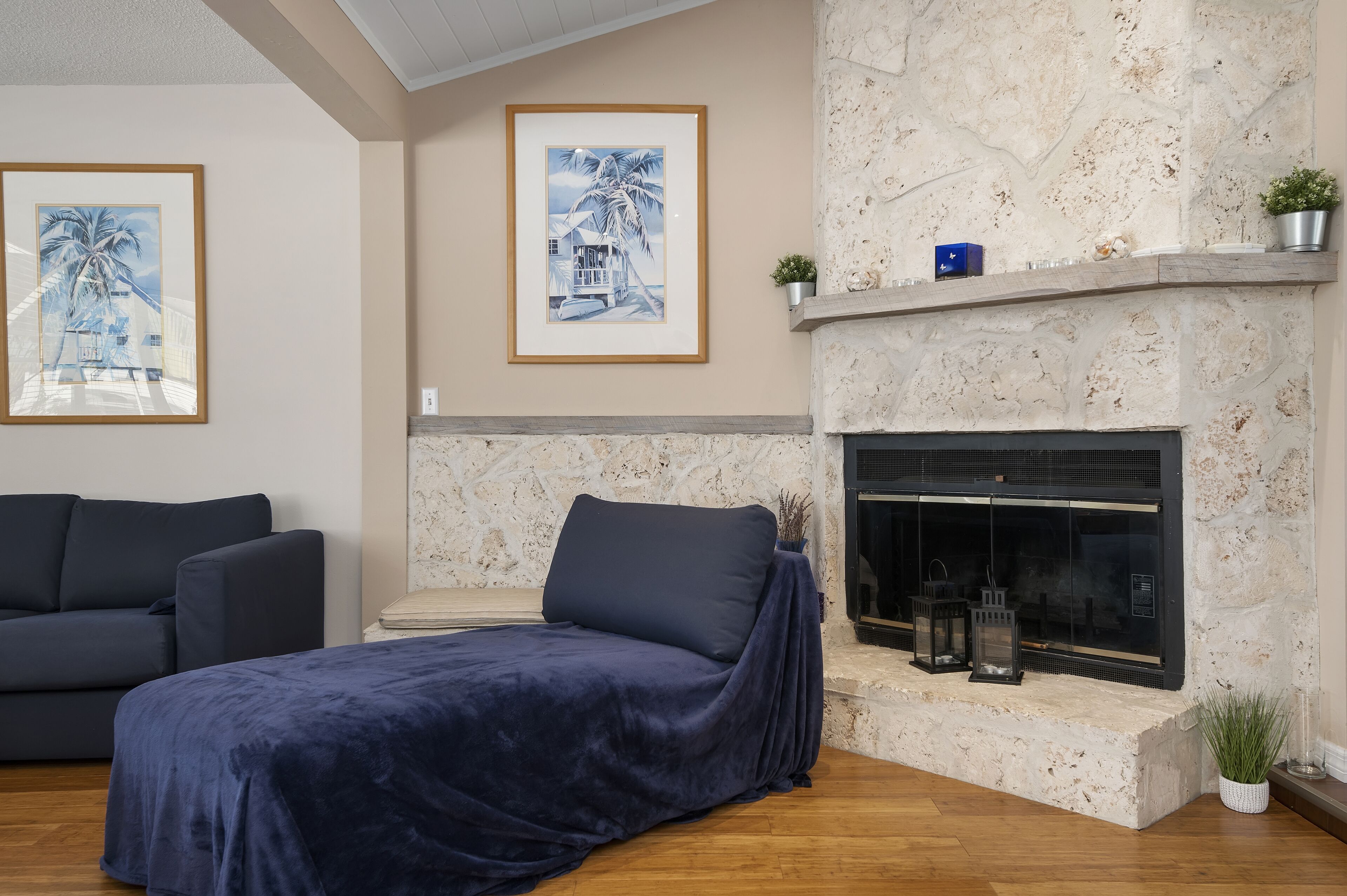 A room with a bed, a sofa, a fireplace, and two framed pictures on the wall.
