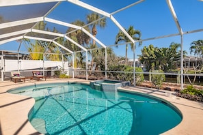 Piscina com cobertura de vidro, rodeada por palmeiras e área de estar coberta.