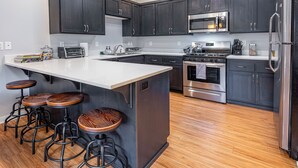 Una cocina moderna con armarios oscuros, una isla grande con taburetes, electrodomésticos de acero inoxidable y suelo de madera.