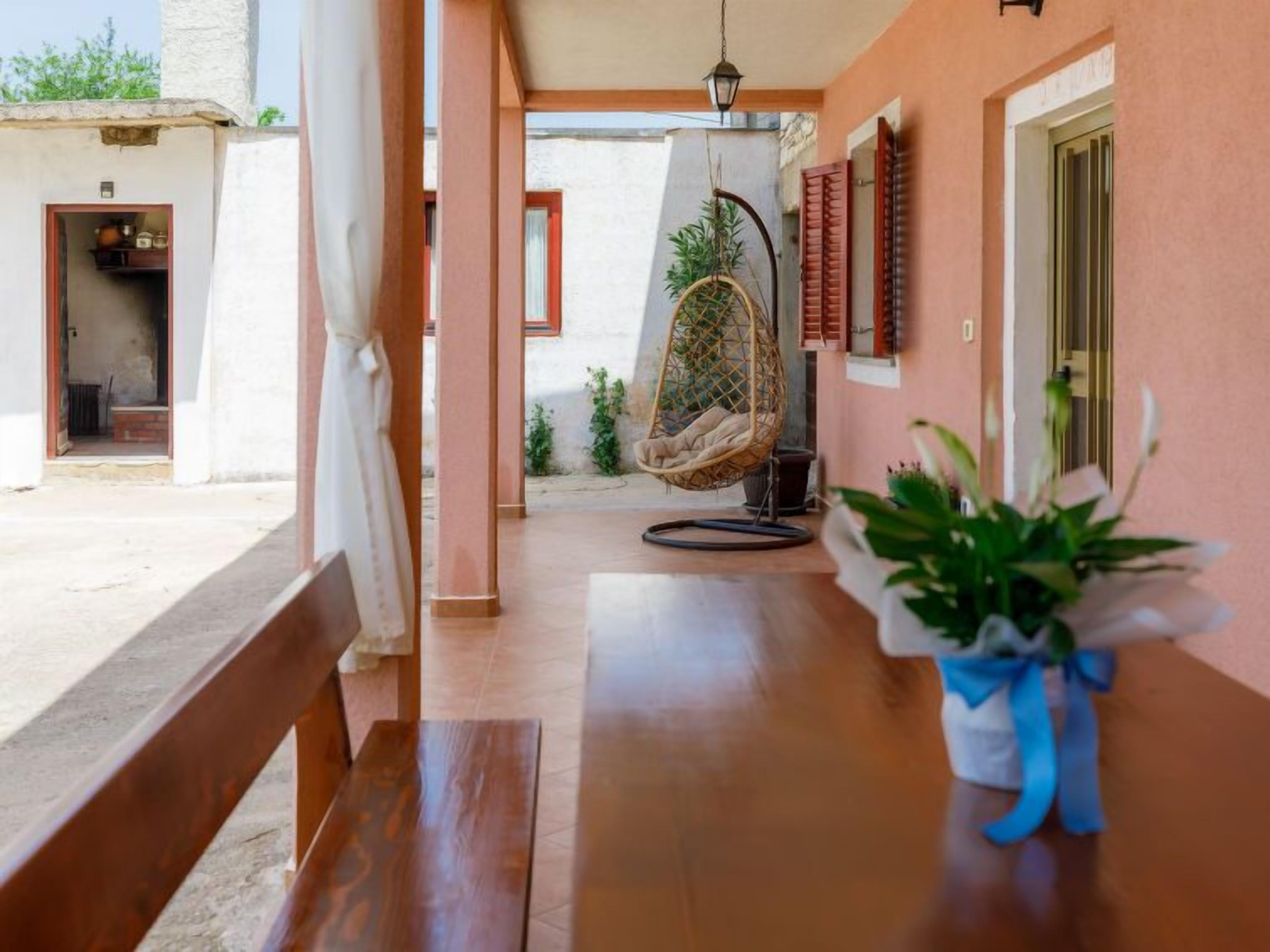 A wooden bench, a hanging chair, and a potted plant on a porch.