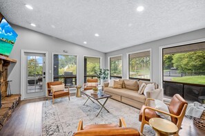 Relax in a spacious room with a seating area, coffee table, and large windows offering views of the backyard and road.