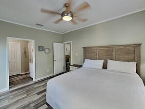 Une chambre à coucher avec un lit, un ventilateur de plafond, une tête de lit en bois et une porte donnant sur une autre pièce.