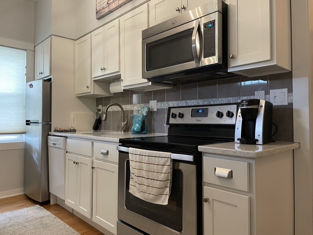 A kitchen with white cabinets, a stainless steel microwave, a stove, and a dishwasher.