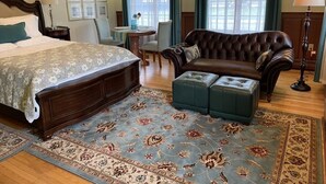A bedroom with a large bed, a leather sofa, a small table, and a chair.