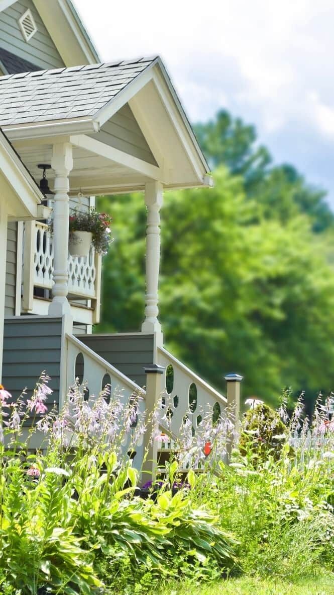 Et hus med en veranda, en lille balkon og en have med forskellige planter og blomster.