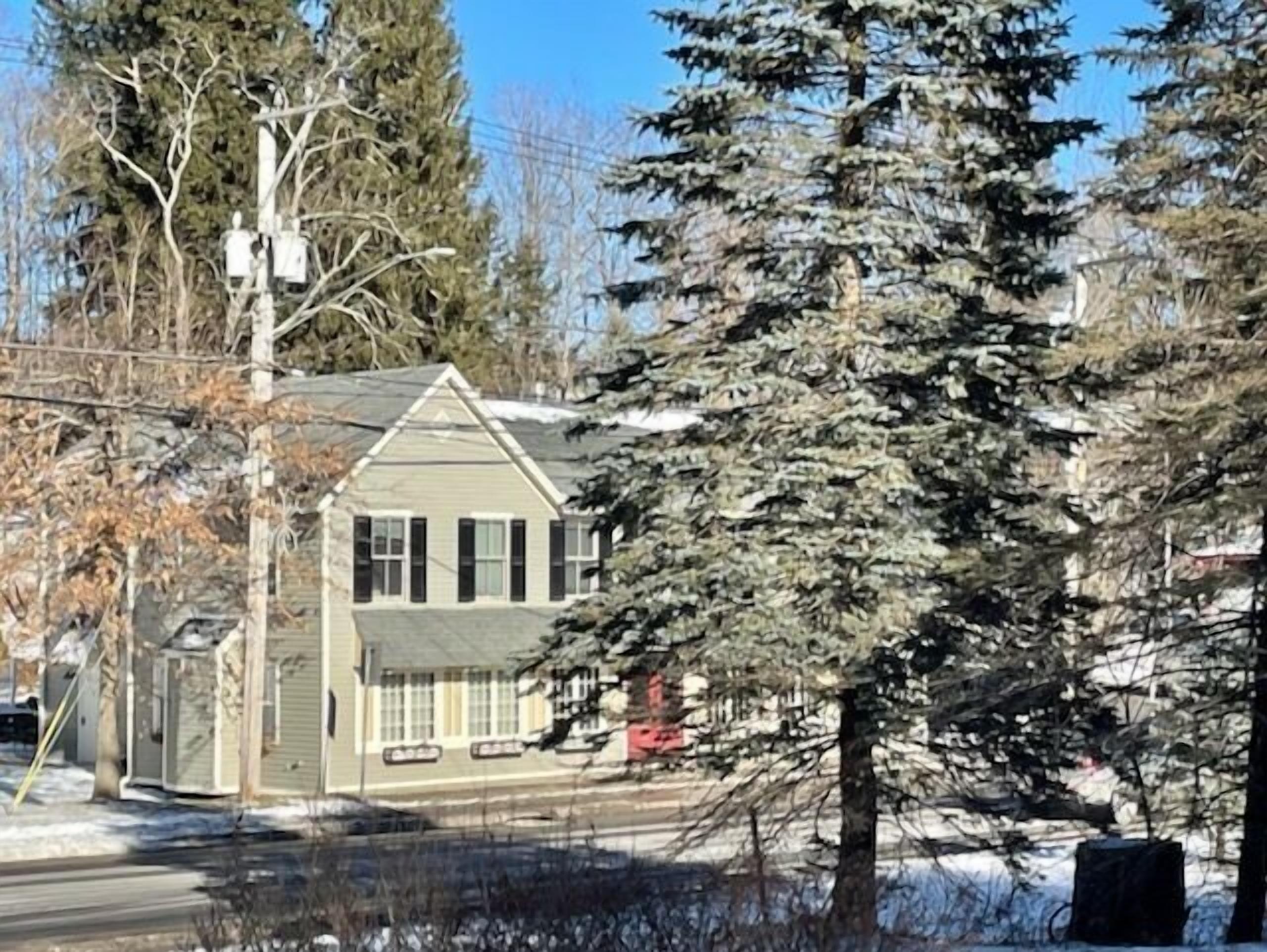 Une maison à deux étages, dotée d’un toit à pignon, entourée d’arbres et recouverte de neige.