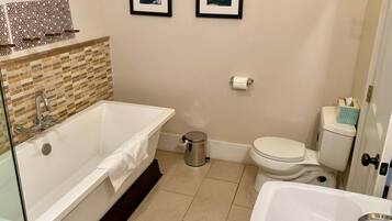Een moderne badkamer met een vrijstaand bad, toilet en wastafel. Twee ingelijste foto's hangen aan de muur.