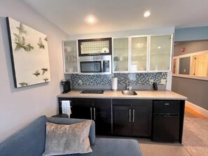 Cocina compacta con microondas, lavamanos y muebles oscuros.