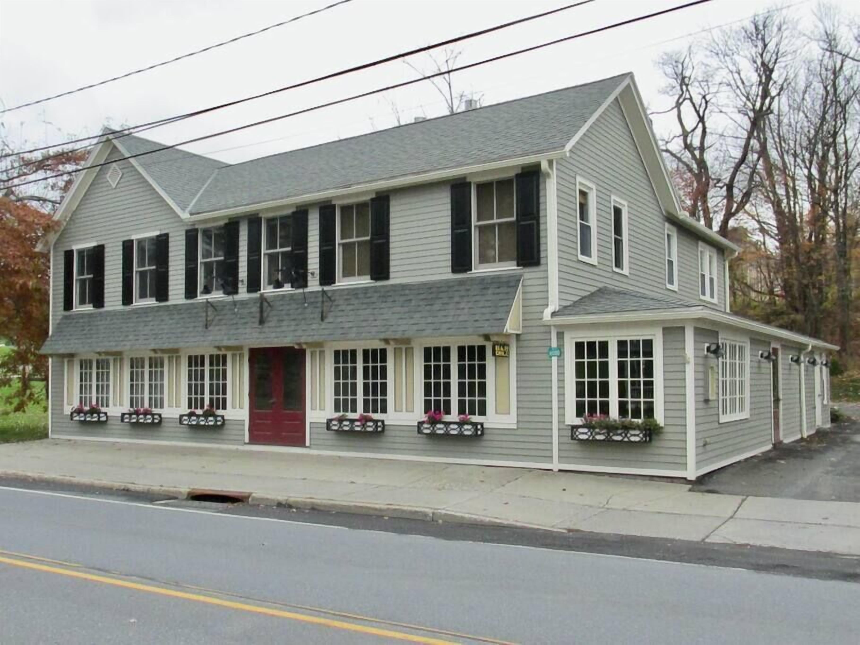 A two-story building with a red front door, multiple windows, and a small porch with potted plants.