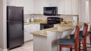 A kitchen with white cabinets, a black refrigerator, a microwave, a stove, and a granite countertop.
