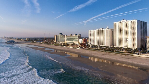 A coastal hotel with multiple high-rise buildings, beachfront access, and a pier extending into the water.