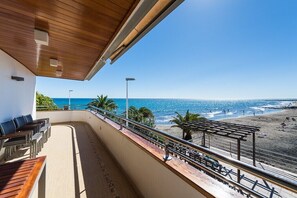 Uma varanda com vista para a praia, mobiliário externo e um pérgola.