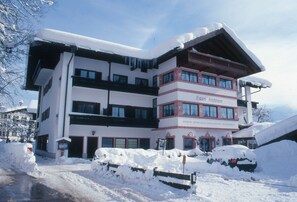 Ein mehrstöckiges Hotel mit verschneitem Dach und Balkonen, eingebettet in eine verschneite Landschaft.