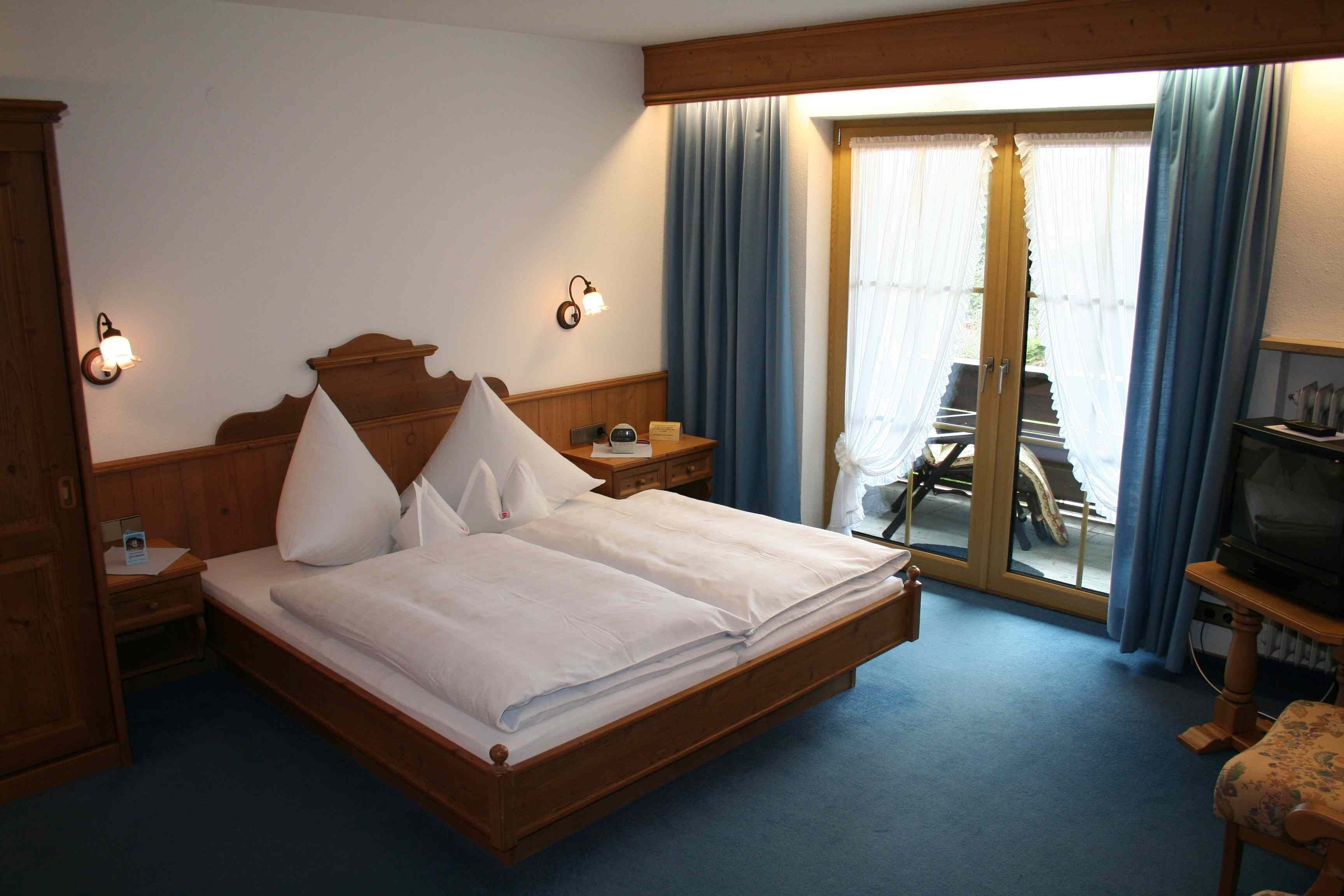 Une chambre d’hôtel avec un lit en bois, une table de chevet, une télévision et une porte-fenêtre coulissante donnant sur un balcon.