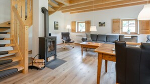 Un amplio salón con escalera de madera, estufa de leña, sofá y mesa de comedor.