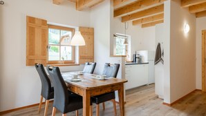 Un comedor con una mesa y sillas de madera, una cocina al fondo y un ventanal con vistas al exterior.