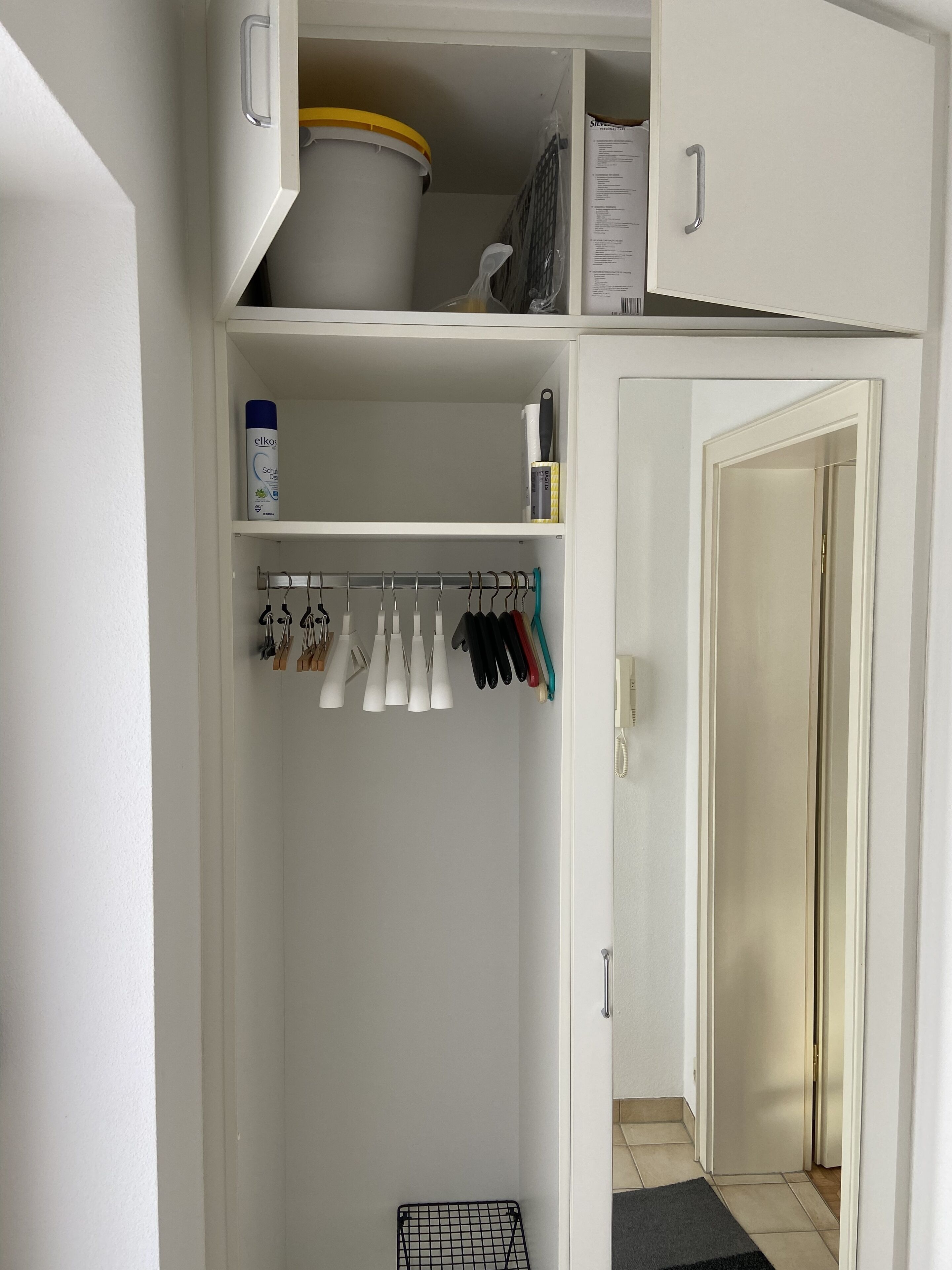 A white closet with hanging clothes, a shoe rack, and a storage bin.