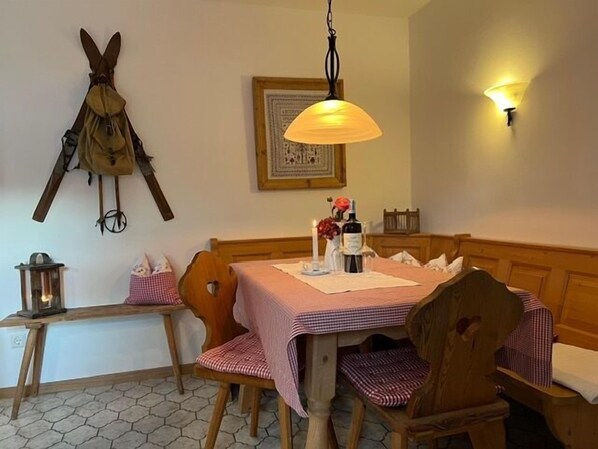 A dining area with a table set for two, wooden chairs, a bench, a wall-mounted lamp, and a framed picture. - Vacation apartment Falkenstein for 2 persons with terrace, 45 sqm, eat-in kitchen (Inzell)