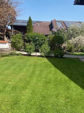 Une pelouse bien entretenue, agrémentée de divers arbres et arbustes, un banc et un bâtiment équipé de panneaux solaires.